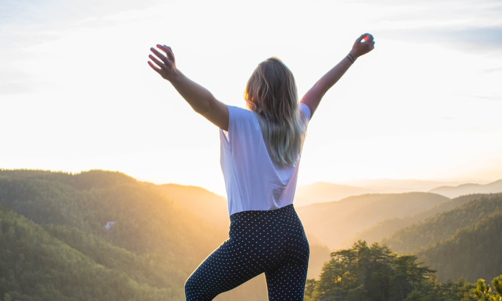 Woman standing on rock with arms up bg