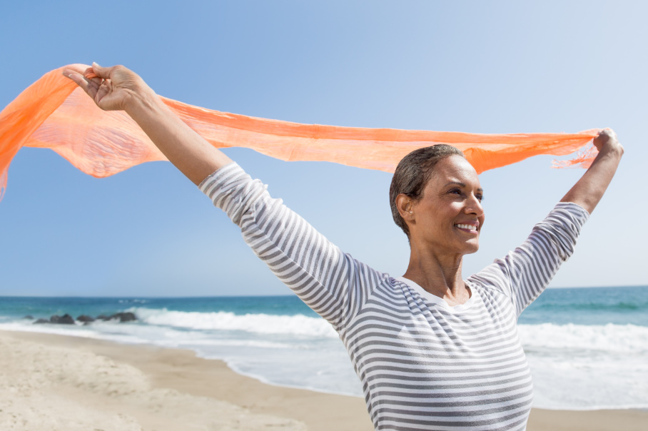 Woman holding orange scarf while standing on beach